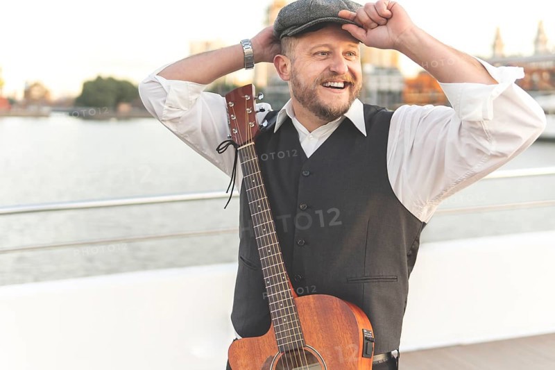 Guitarist posing on a bridge over a river with his guitar