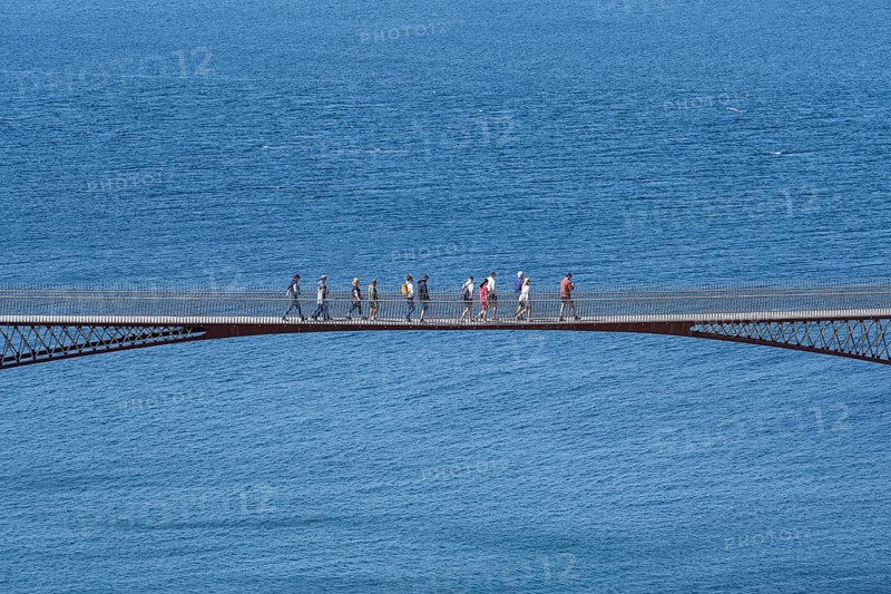 Tourists walk across the new footbridge to the peninsula with the castle ruins of Tintagel Castle
