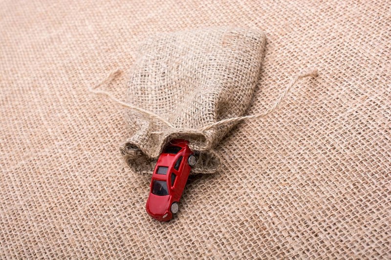 Red toy car coming out of a linen sack on a linen canvas