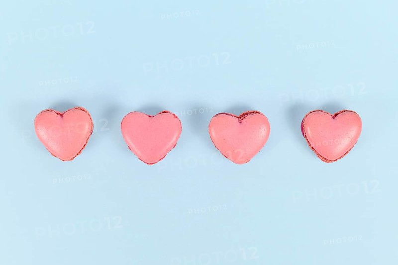Heart shaped French macaron sweets in a row on blue background