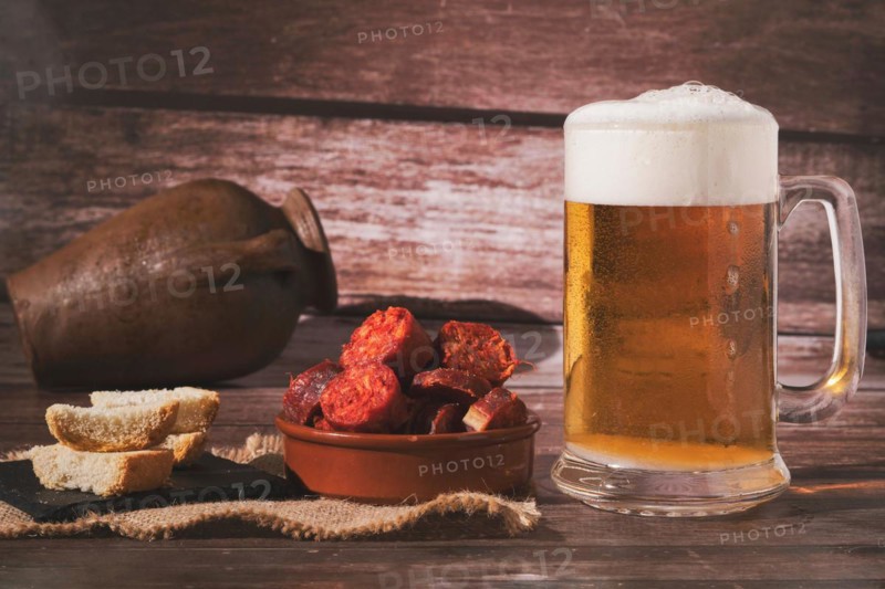 Mug of fresh beer with foam and clay pot with bread and chorizo sausage