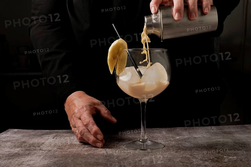 Waitress dressed in black serving a banana cocktail with ice and a slice of banana with a cocktail shaker