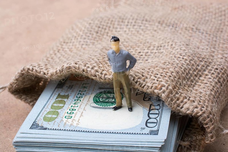 Man figurine standing on bundle of US dollar in a sack