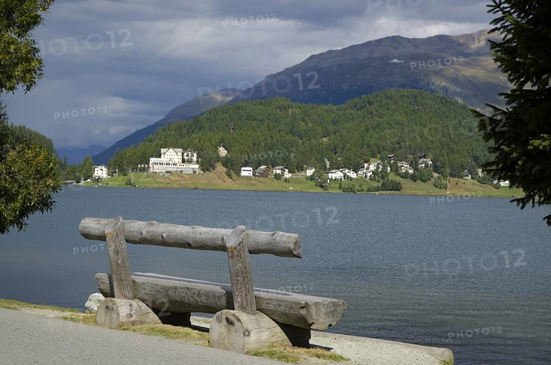 Wood Bench and Trees on St Moritz Lake with Mountain and Grey Clouds in a Sunny Day in Switzerland