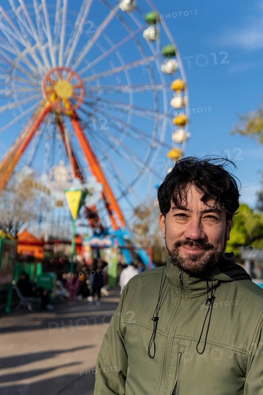 Portrait of latino man in an amusement park posing happy with the ferris wheel in the background
