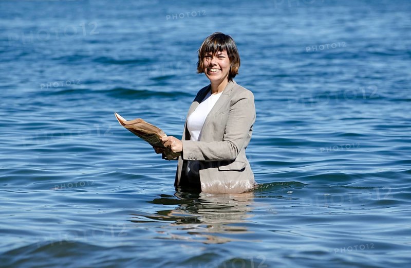 Elegant Business Woman with Suit Standing in the Water and Reading a Newspaper
