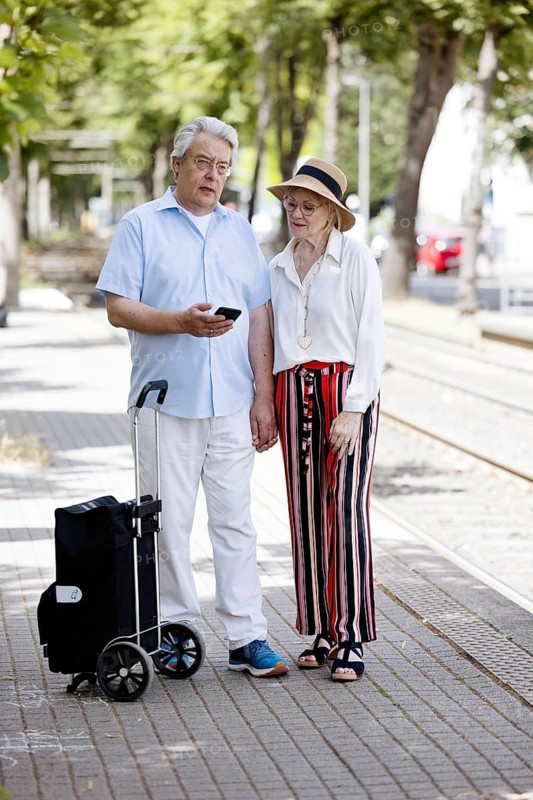 Elderly couple waiting for the tram at a stop with a smartphone in hand