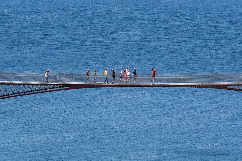 Tourists walk across the new footbridge to the peninsula with the castle ruins of Tintagel Castle