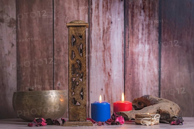 Wooden incense burner with colored candles and Tibetan bowl on a wooden background