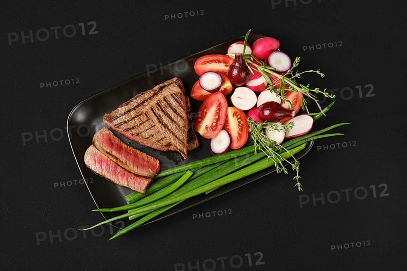Top view of grilled tri-tip loin beef steaks medium rare with fresh vegetables on black background
