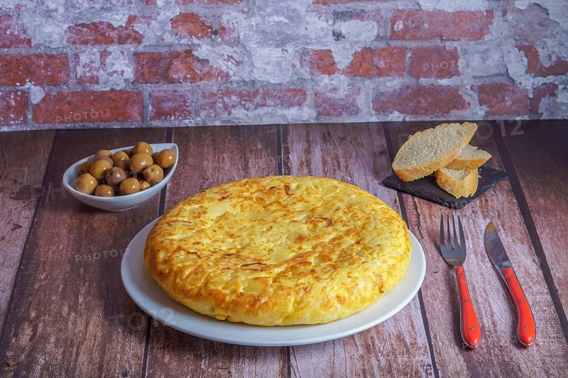 Typical spanish potato omelette freshly made on a wooden table with cutlery