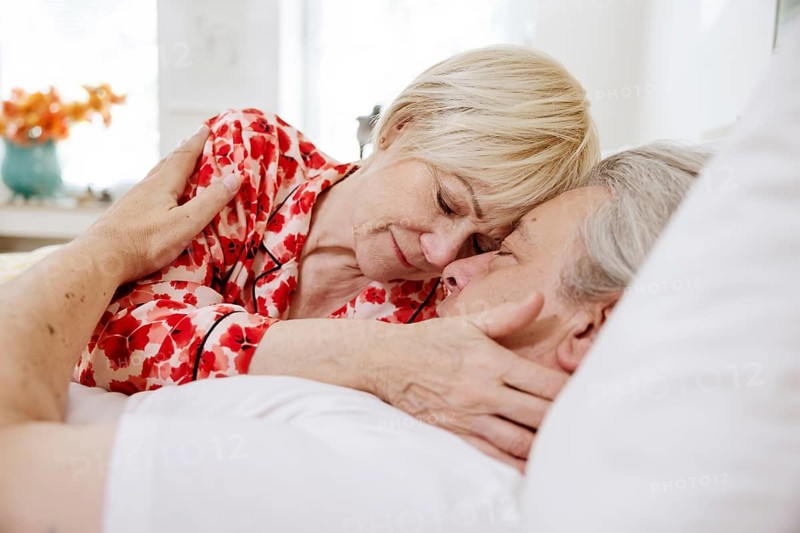 Elderly couple lying together in bed in bedroom embracing tenderly