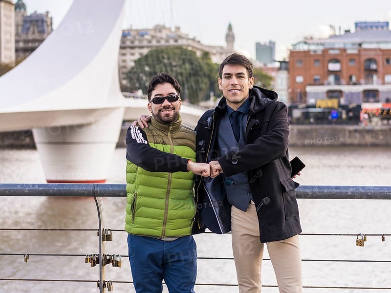 Two male friends hugging while looking at camera near Puente de la Mujer
