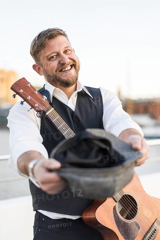 A smiling street musician looking at camera and carrying his guitar while asking for tips