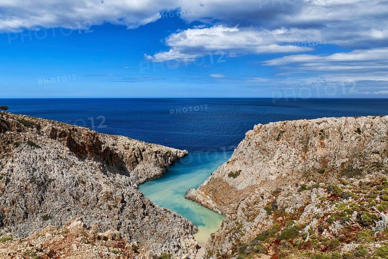 Beautiful view of z-shaped cove or lagoon in typical hills of Crete landscape. Clear blue sky and beautiful clouds on sunny day. Azure sea waters. Stefanou beach