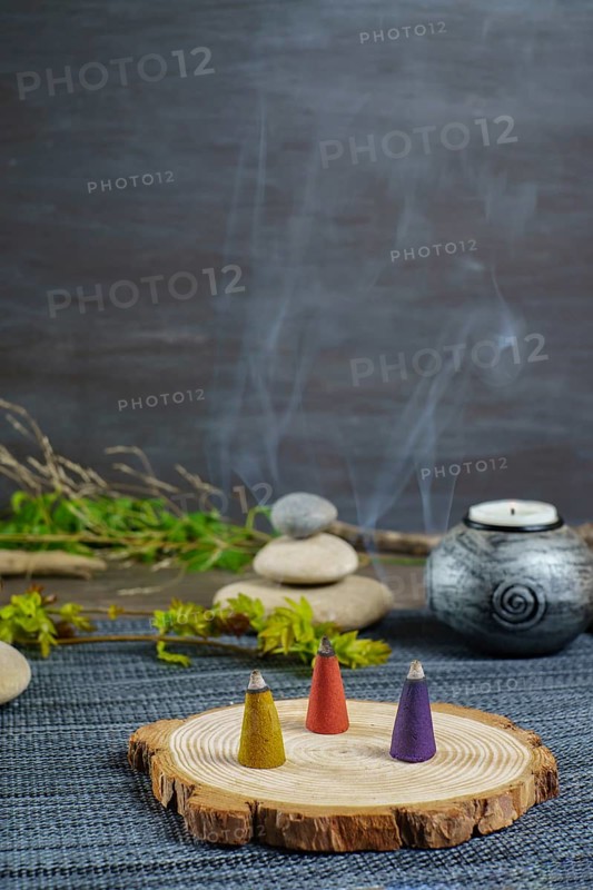 Colorful incense cones on a wooden disk with candles and zen stones stacked on top of them