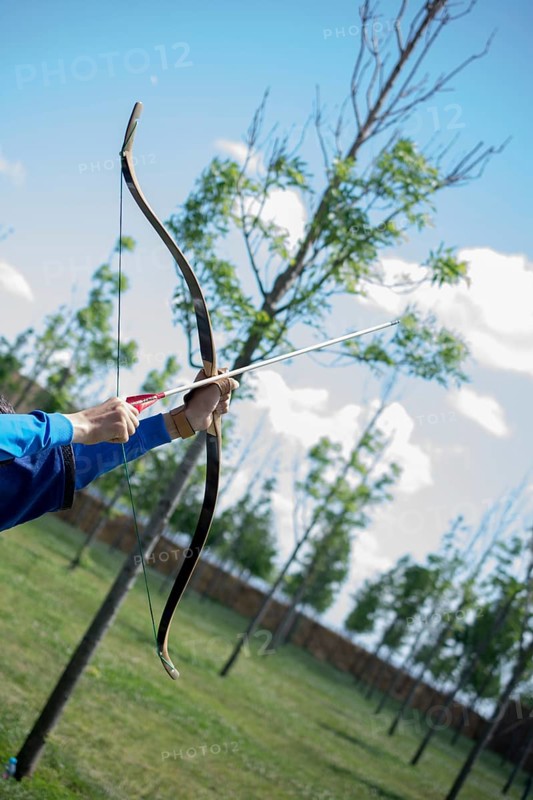 Archer with bow in traditional clothes shooting an arrow