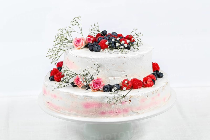 Summery fresh two tier wedding cake decorated with berries and flowers festive cream cake on light background