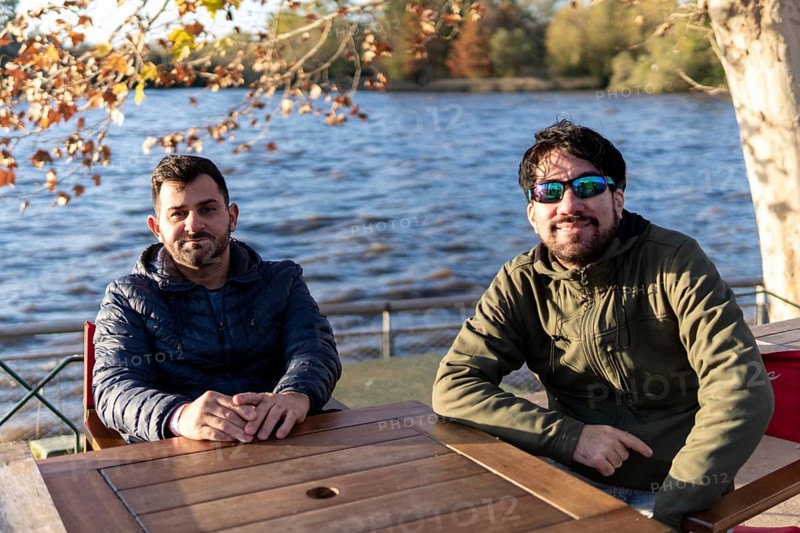 Two friends sitting at an outdoor bar on a river at sunset