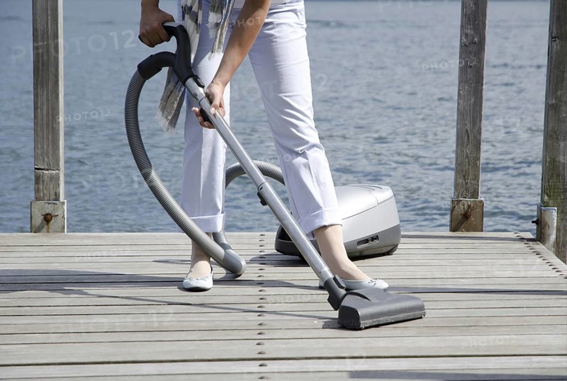 Woman Using Vacuum Cleaner the Pier over the Alpine Lake with Cleaning Equipment in Switzerland