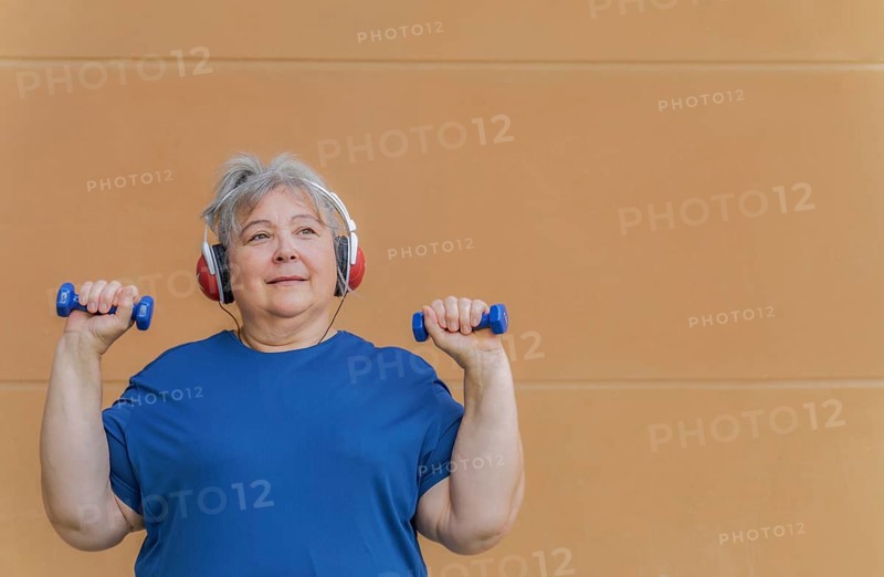 White haired obese older woman exercising with dumbbells and headphones listening to music for weight loss .isolated on orange background and copy space