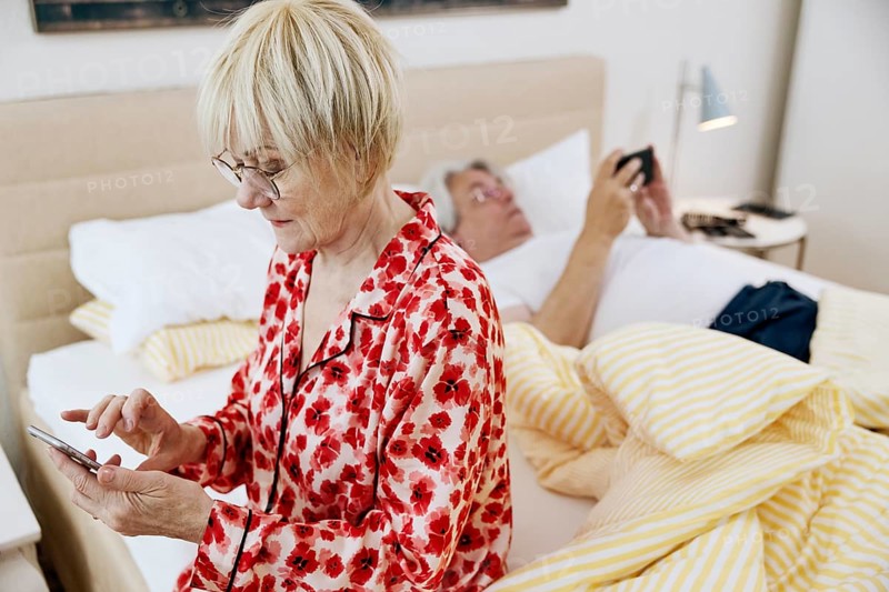 Elderly couple together in the bedroom and each looking at their own smartphone
