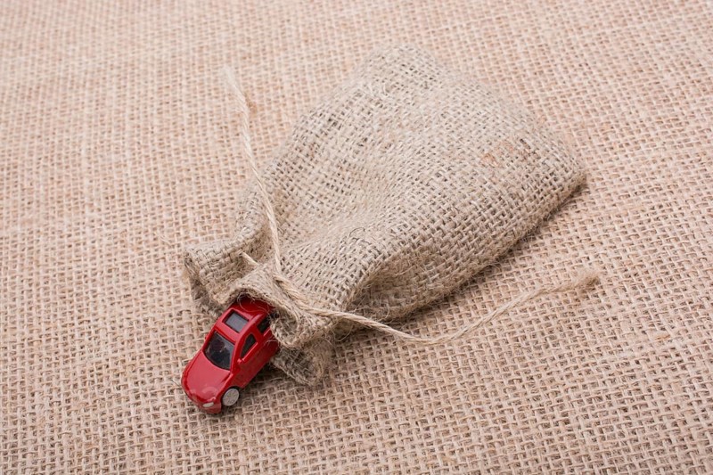 Red toy car coming out of a linen sack on a linen canvas