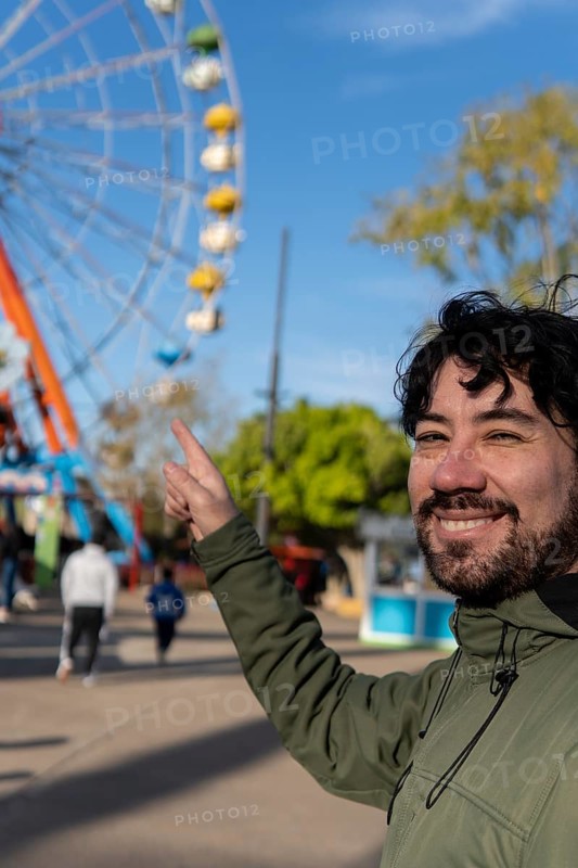 Portrait of latino man in an amusement park posing happy with the ferris wheel in the background