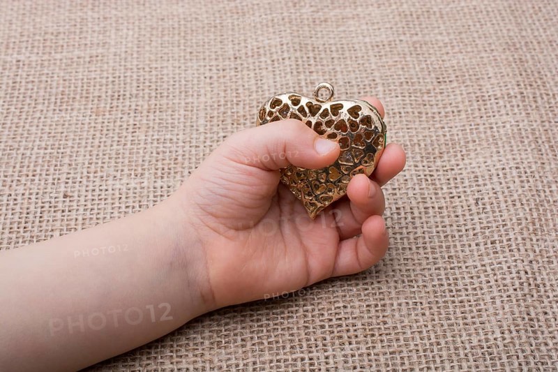 Heart shaped gold color metal object in hand