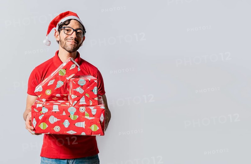 Christmas man portrait holding gift boxes and smiling isolated. Smiling guy in santa hat holding christmas gift boxes. Friendly man in christmas clothes holding gift boxes isolated