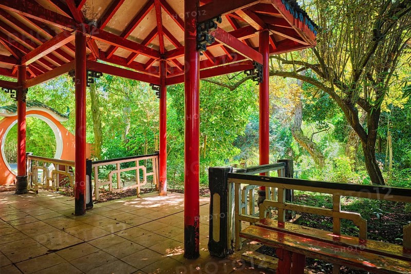 Red Chinese style pavilion in lush greenery of asian part of tropical botanical garden in Lisbon