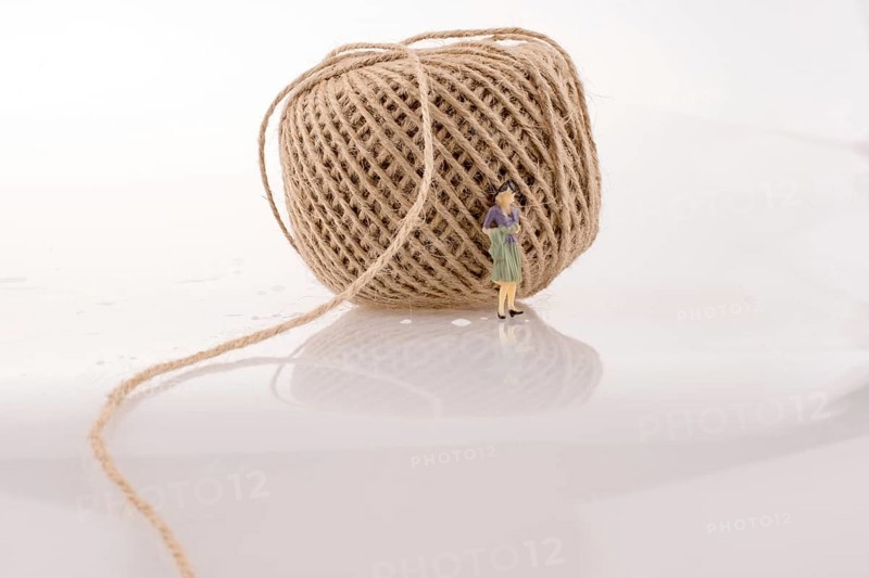 Woman figure beside a linen spool of thread on a white background