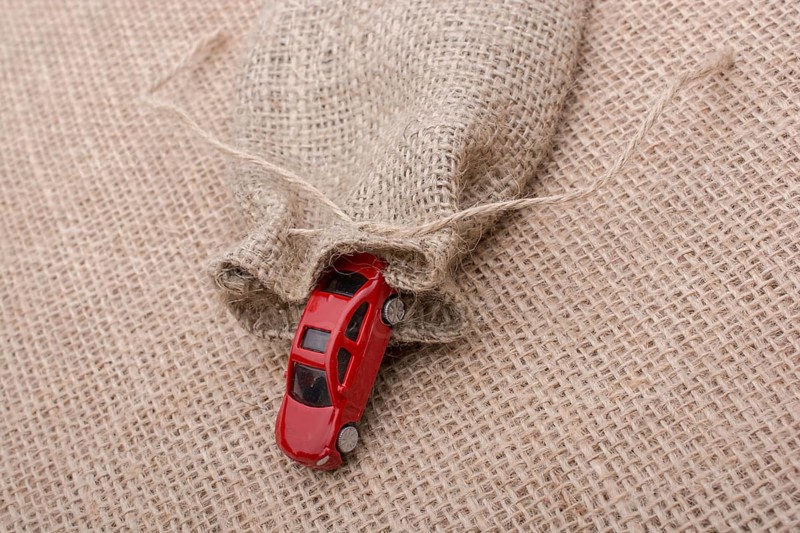 Red toy car coming out of a linen sack on a linen canvas