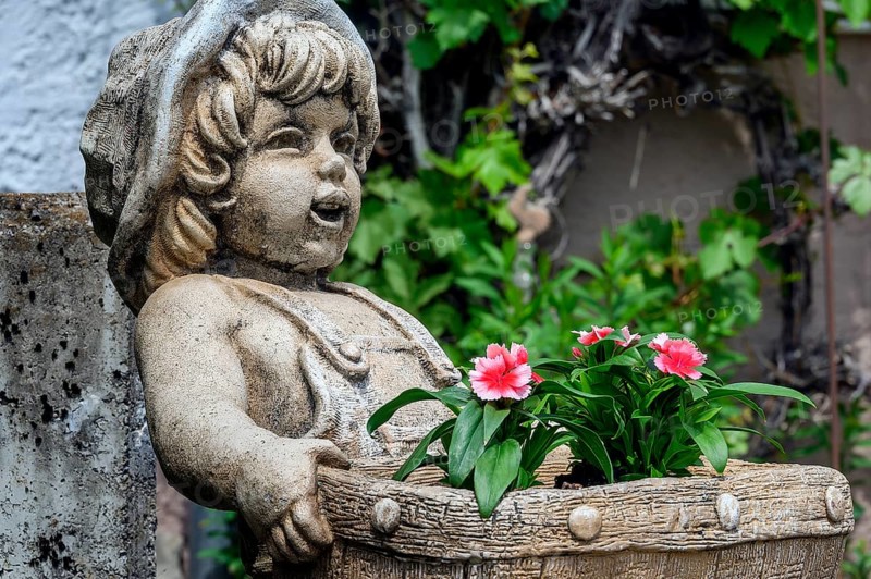 Childlike stone figure with flower basket and garden carnations