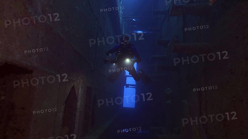 Scuba diver with lantern floats inside of ferry Salem Express shipwreck