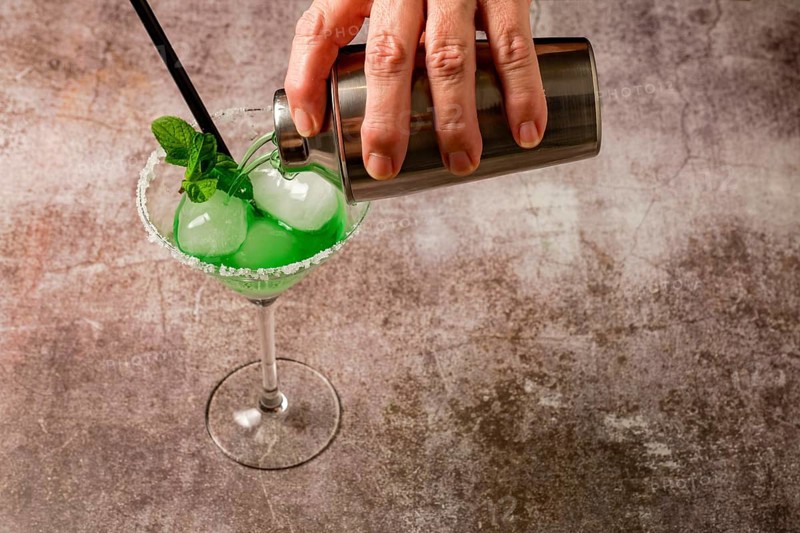Hand of a woman serving a mint cocktail with ice straw and mint leaves with a cocktail shaker