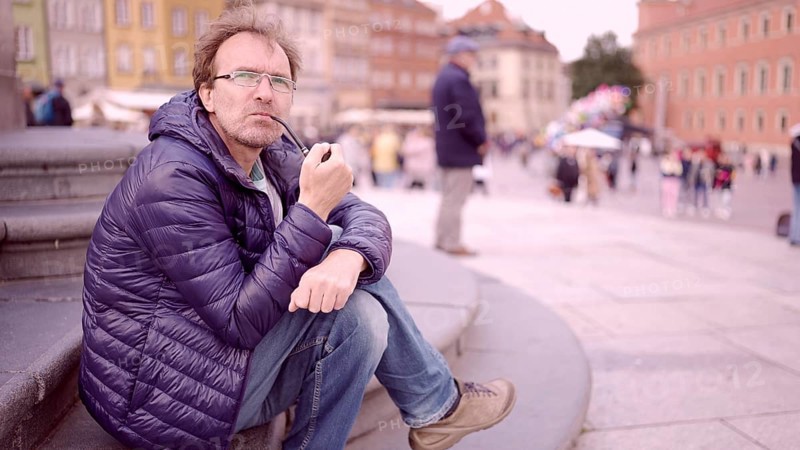 Adult man sitting on square and smoking a tobacco pipe in the Palace Square