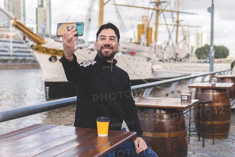 Latin tourist drinking coffee and taking a selfie at an outdoor bar in Puerto Madero