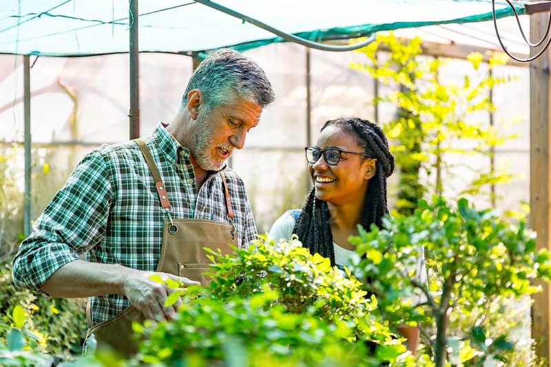 Master gardener teaching student girl flower nursery in greenhouse