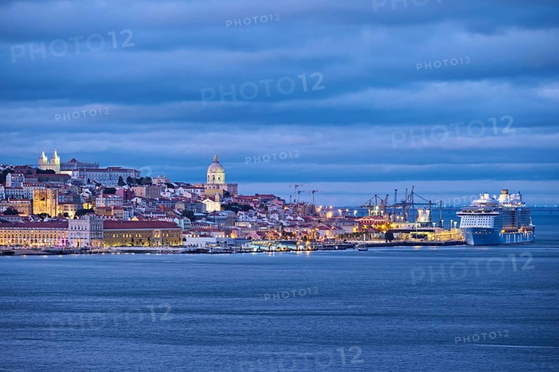 View of Lisbon over Tagus river with passing ferry boat from Almada with moored cruise liner in evening twilight. Lisbon