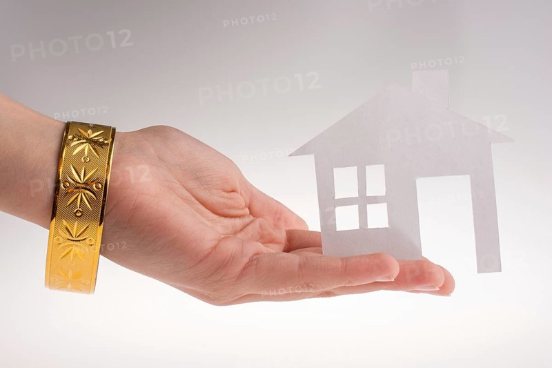 Hand holding a paper house with a golden bracelet