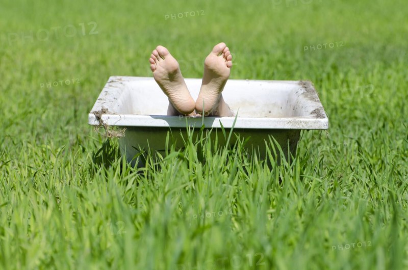 Woman lying in a bathtub on a green field