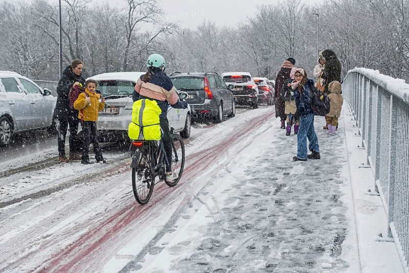 Cyclist and children walking to school over slippery pavement on bridge covered in sleet during unexpected late snow shower in March