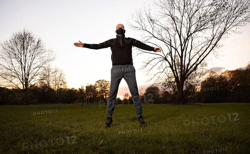 Man with mask stretches in a meadow in autumn.