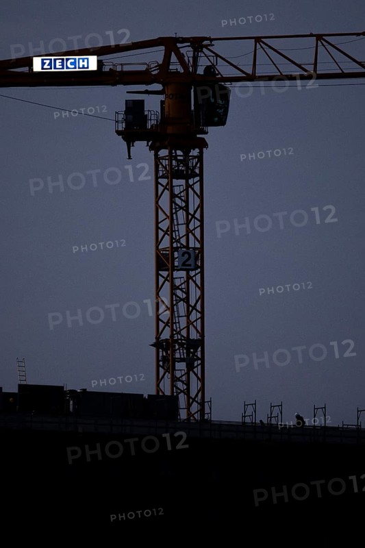 A worker draws on scaffolding and in front of a crane on a newly built house