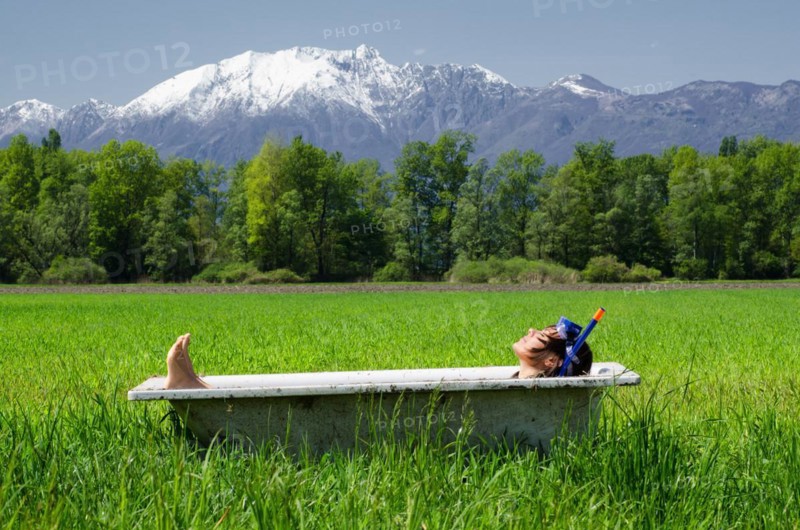 Woman lying in a bathtub on a green field with grass and trees