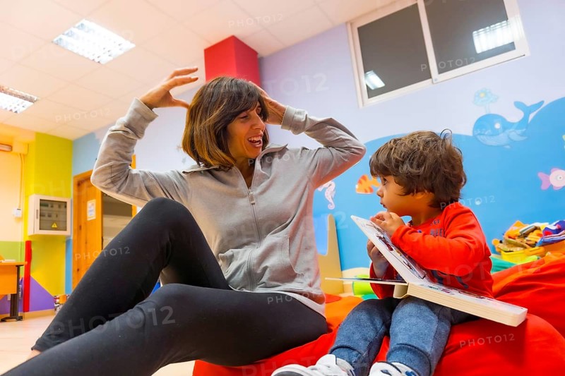 Woman teacher with a child sitting reading a book and expressing things from the story