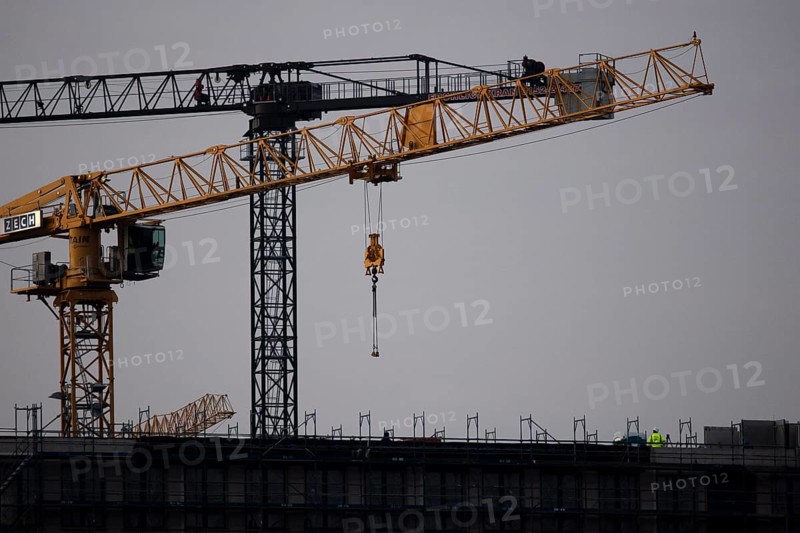 A worker draws on scaffolding and in front of a crane on a newly built house