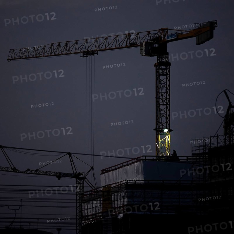 A worker draws on scaffolding and in front of a crane on a newly built house