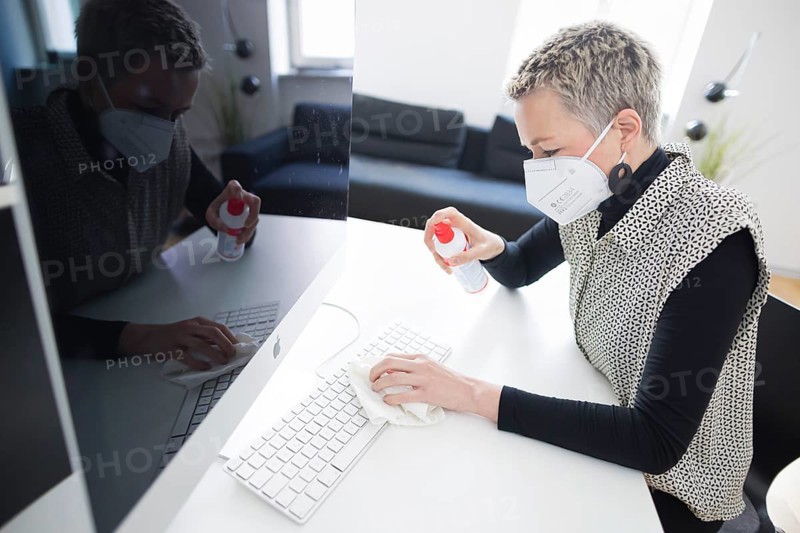 Hygiene at the workplace. A woman disinfects the keyboard at her workplace with disinfectant spray. Berlin
